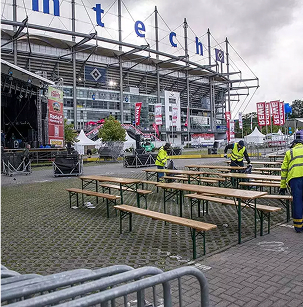 Menschen in Warnwesten stehen bei Bierzeltgarnituren vor dem HSV Stadion