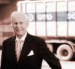 Älterer Mann in Anzug steht vor einem Lkw mit Container im Hintergrund.