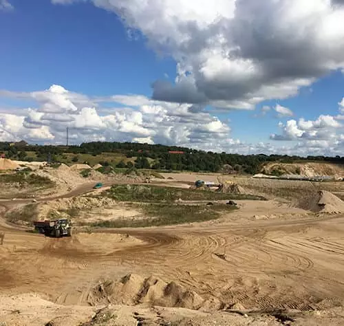 Blick auf eine Baustelle mit Baggern und Sand unter einem bewölkten Himmel.