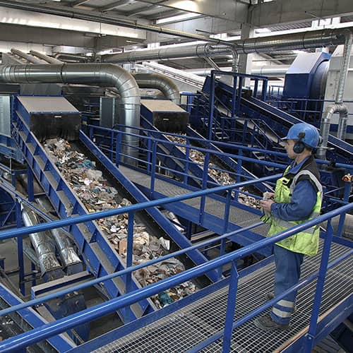 Mitarbeiter in einer Recyclinganlage überwacht Förderbänder mit Abfallmaterialien.