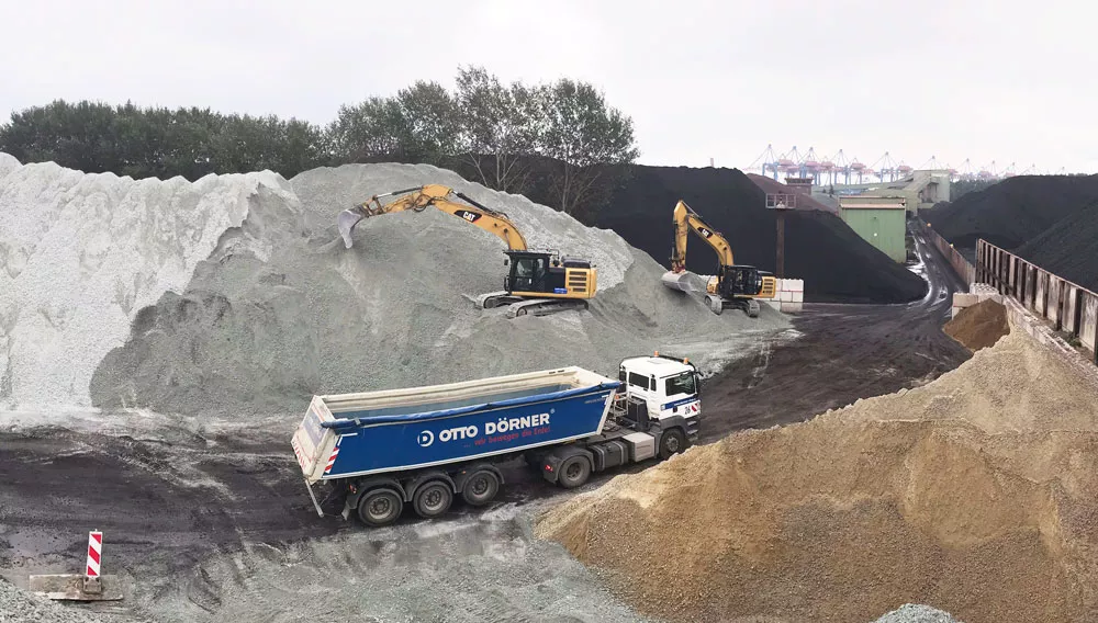 Bauarbeiten mit Baggern und Lkw auf einer Baustelle mit verschiedenen Materialien.