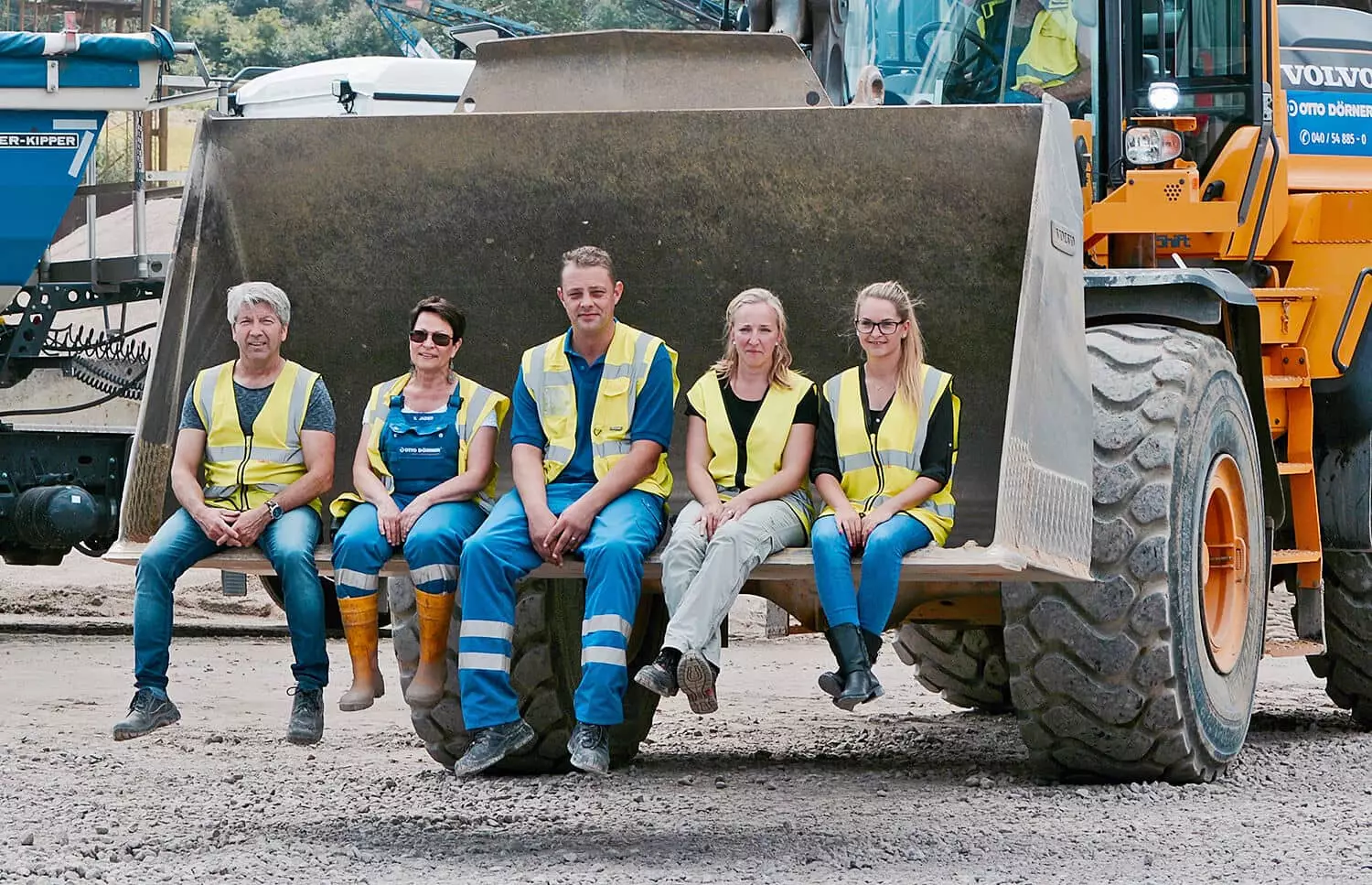Gruppenfoto von Bauarbeitern in Arbeitskleidung auf einem Baggerlader-Sitz.