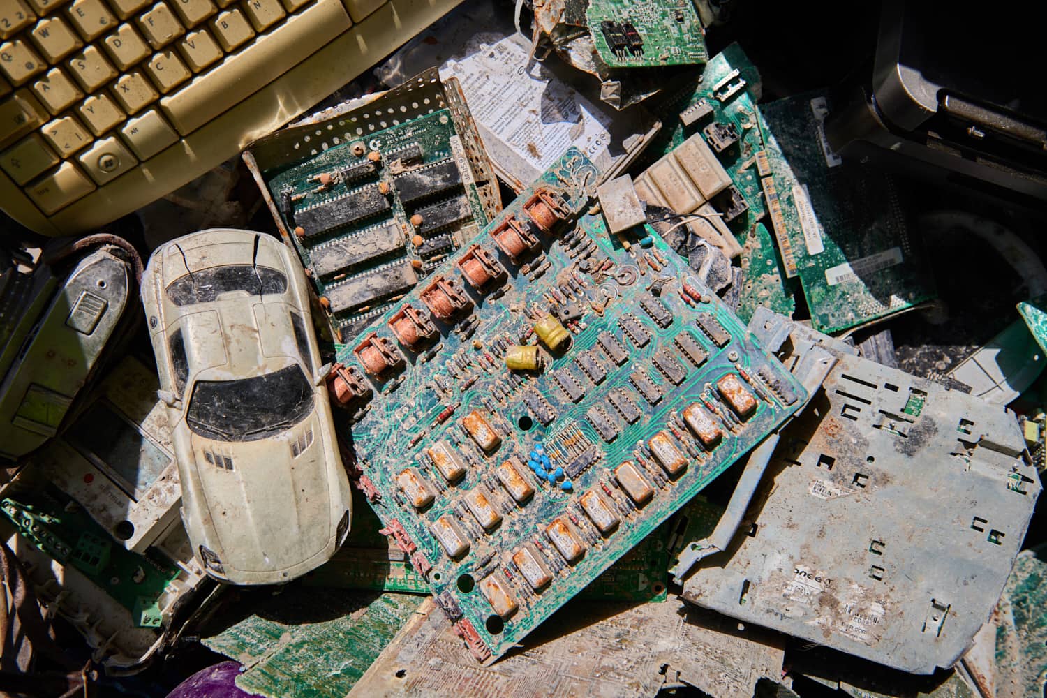 Verschrottete Elektronik mit einer Leiterplatte und Spielzeugautos auf einem Tisch.