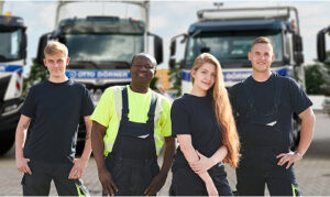 Vier Fachkräfte in Arbeitskleidung vor Lkw, lächelnd und bereit für den Einsatz.