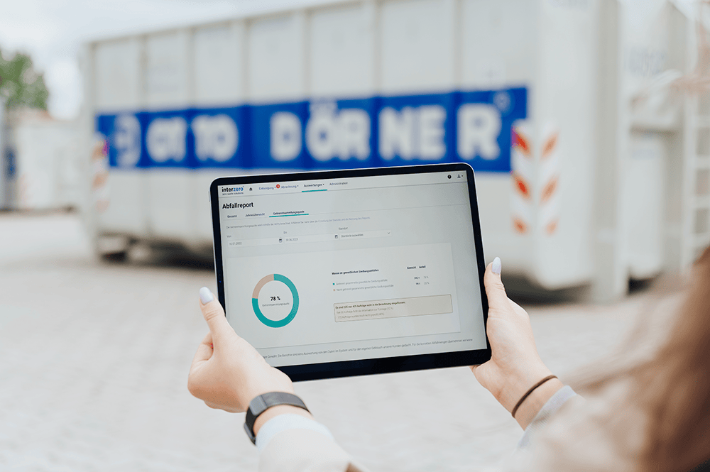 Person h&auml;lt ein Tablet mit einer Analyse-Anwendung vor einem Container im Hintergrund.