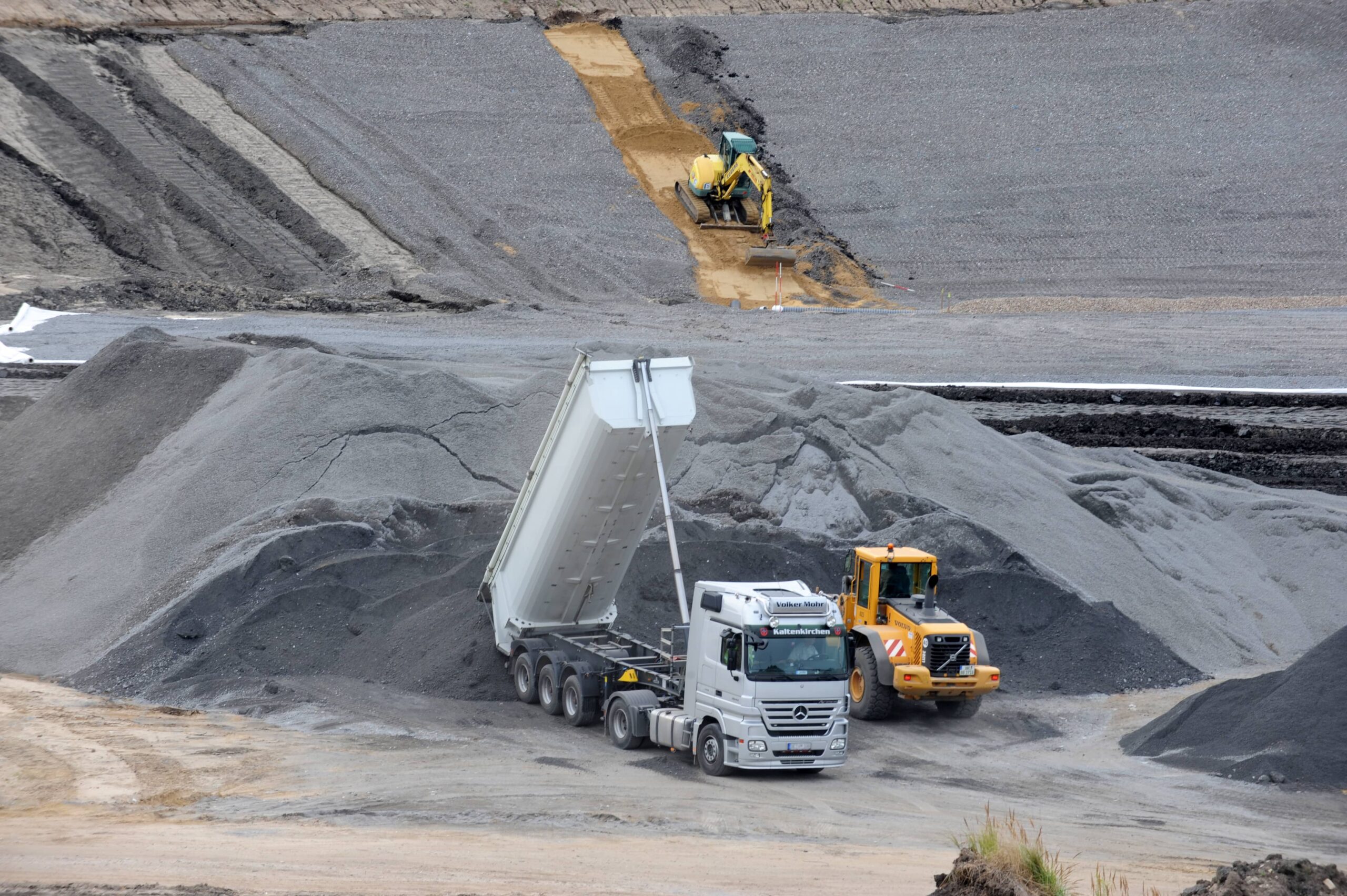Lkw kippt Material ab, w&auml;hrend ein Bulldozer auf einer Baustelle arbeitet.