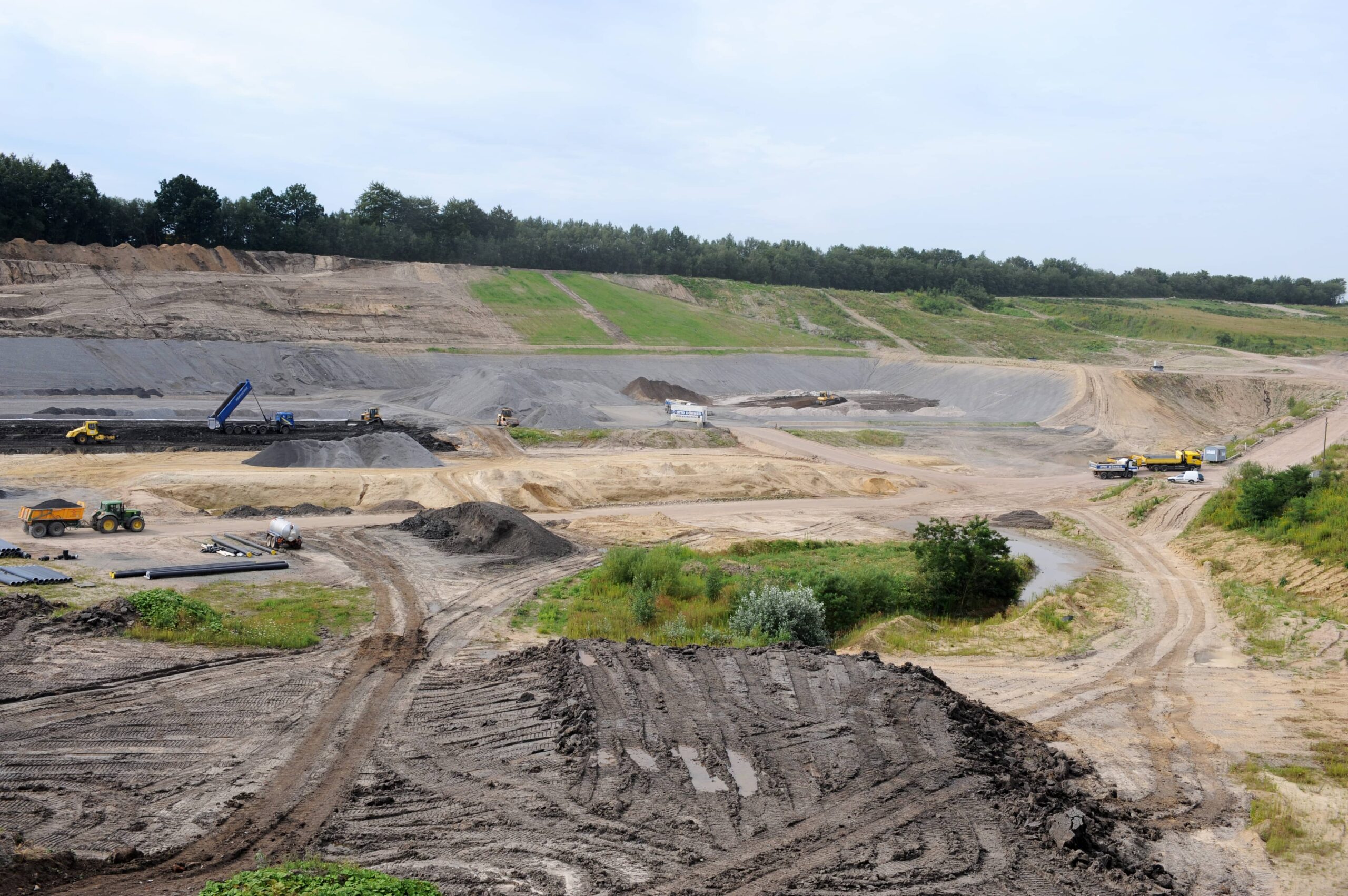 Blick auf eine Baustelle mit Erde, Ger&ouml;ll und Vegetation im Hintergrund.