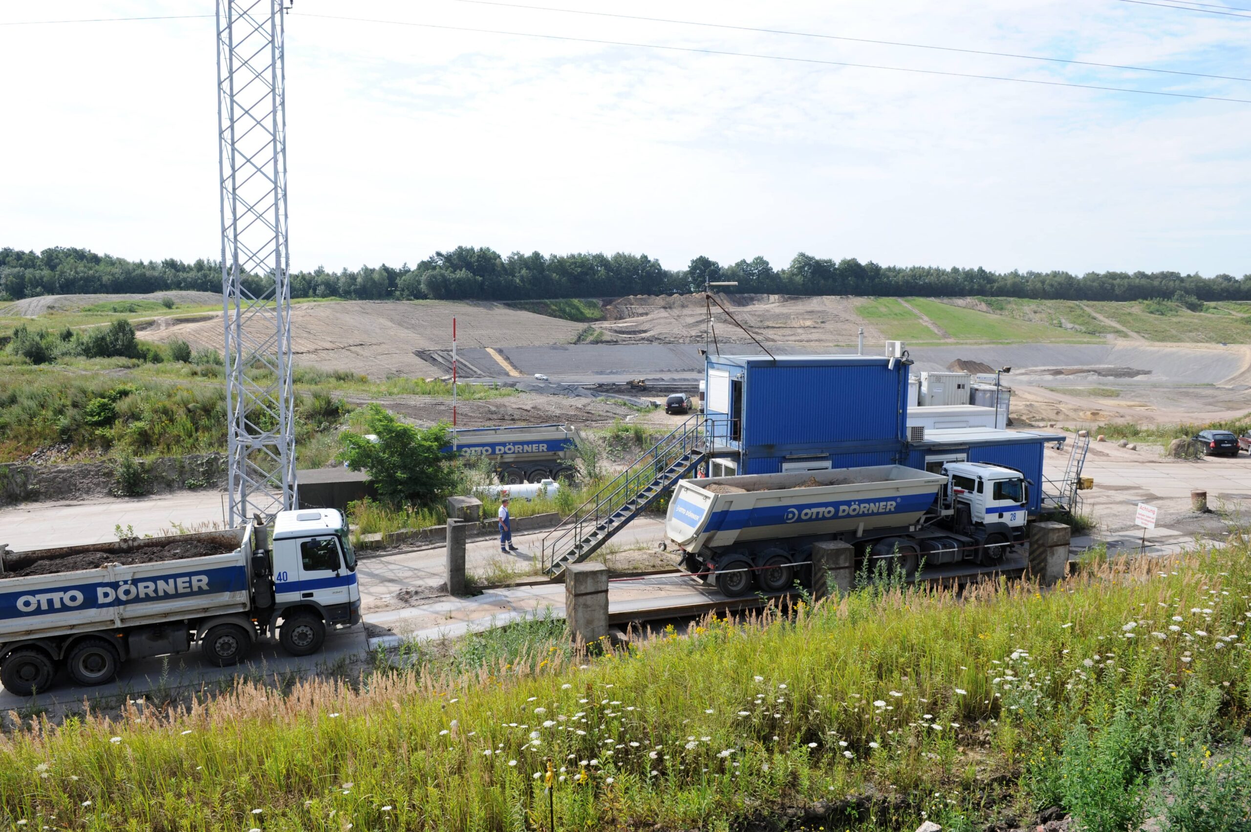 Bauger&auml;te und Lkw auf einer Baustelle mit gr&uuml;ner Umgebung und weitem Gel&auml;nde im Hintergrund.