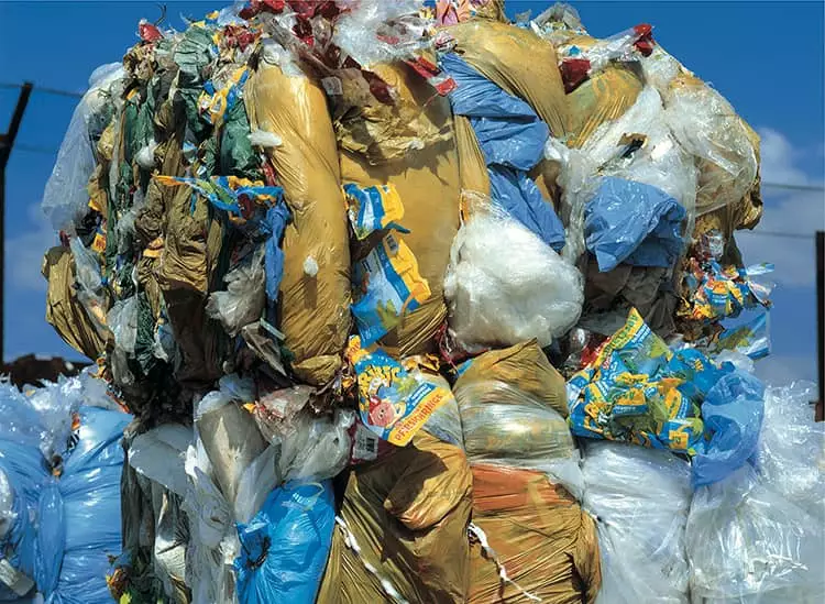 Berg aus verpacktem M&uuml;ll, bestehend aus bunten Plastikt&uuml;ten und Abf&auml;llen unter blauem Himmel.